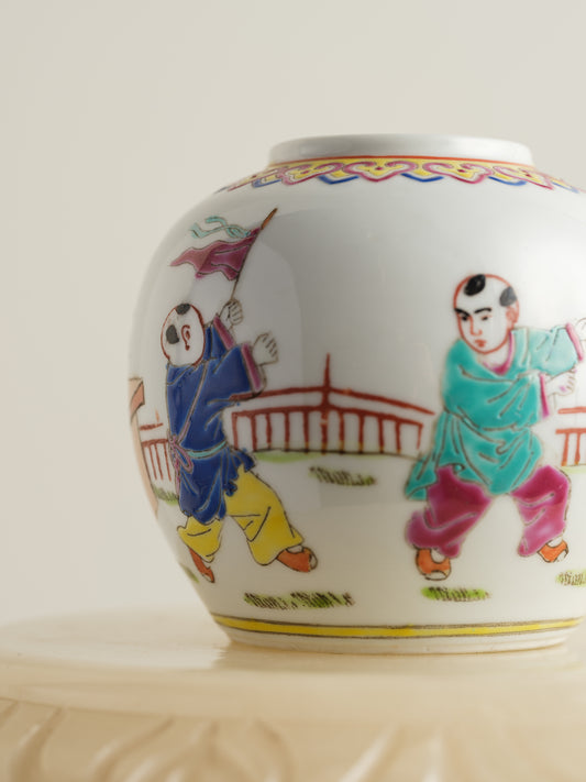 Small porcelain jar hand-painted with playful courtyard children in bright traditional robes.