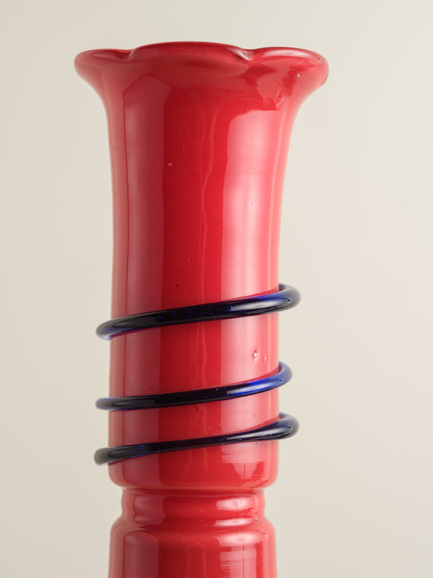 Red glass bud vase with flared rim and cobalt spiral accent wrapping around the neck.
