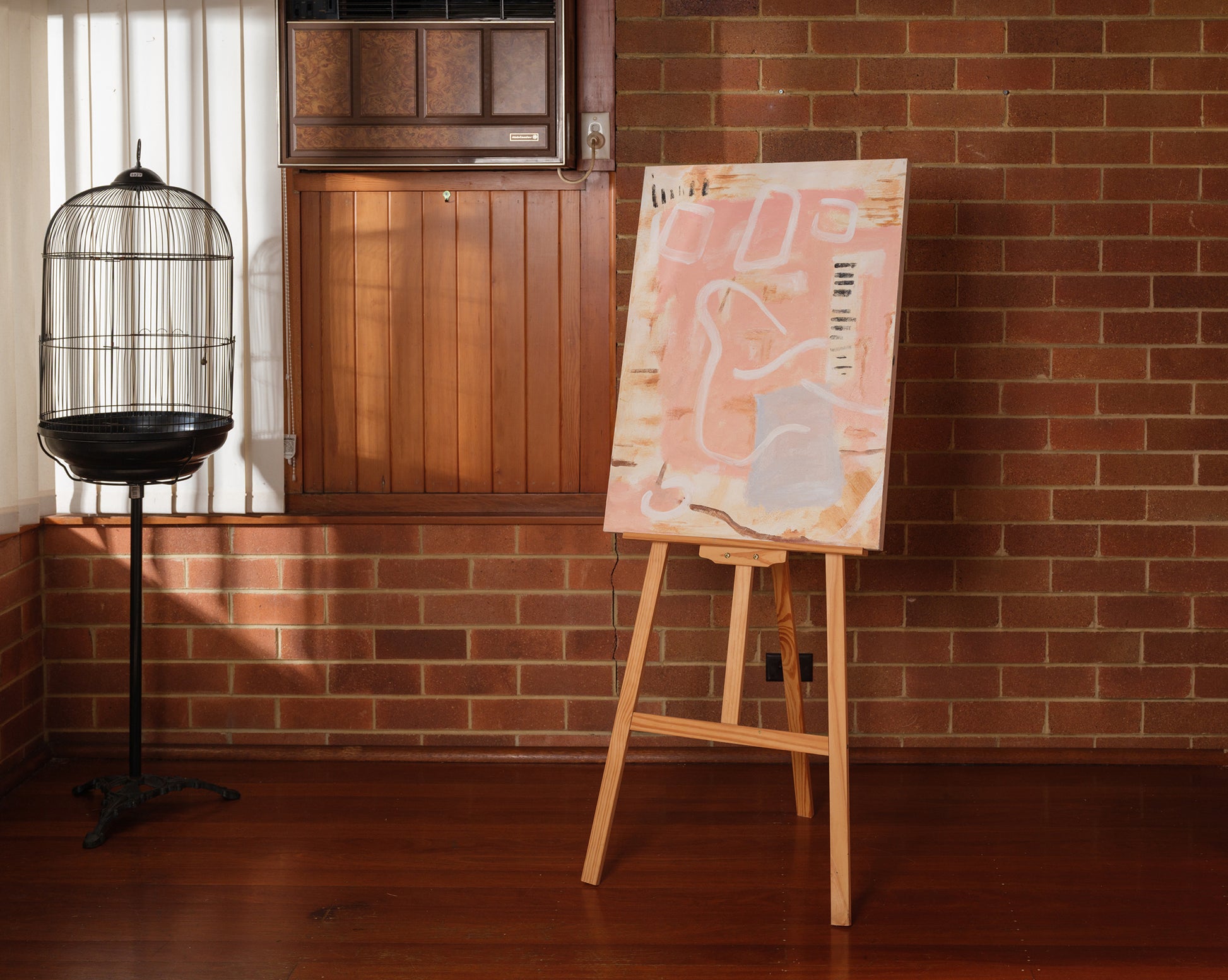 Abstract painting titled Drift in Pink, featuring soft pink and beige tones on canvas, displayed on wooden easel.