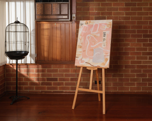 Abstract painting titled Drift in Pink, featuring soft pink and beige tones on canvas, displayed on wooden easel.