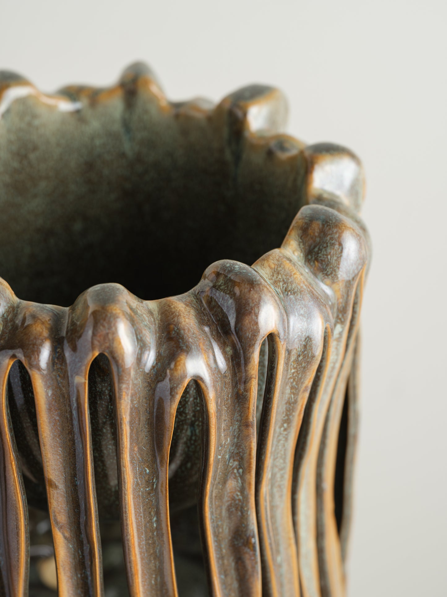 Ceramic vessel titled Drip Cage Vessel, featuring vertical dripping glaze lines forming an openwork cage-like structure with earthy brown and blue tones.