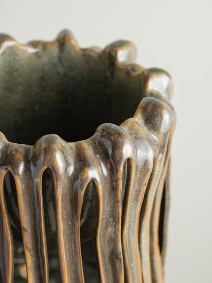 Ceramic vessel titled Drip Cage Vessel, featuring vertical dripping glaze lines forming an openwork cage-like structure with earthy brown and blue tones.
