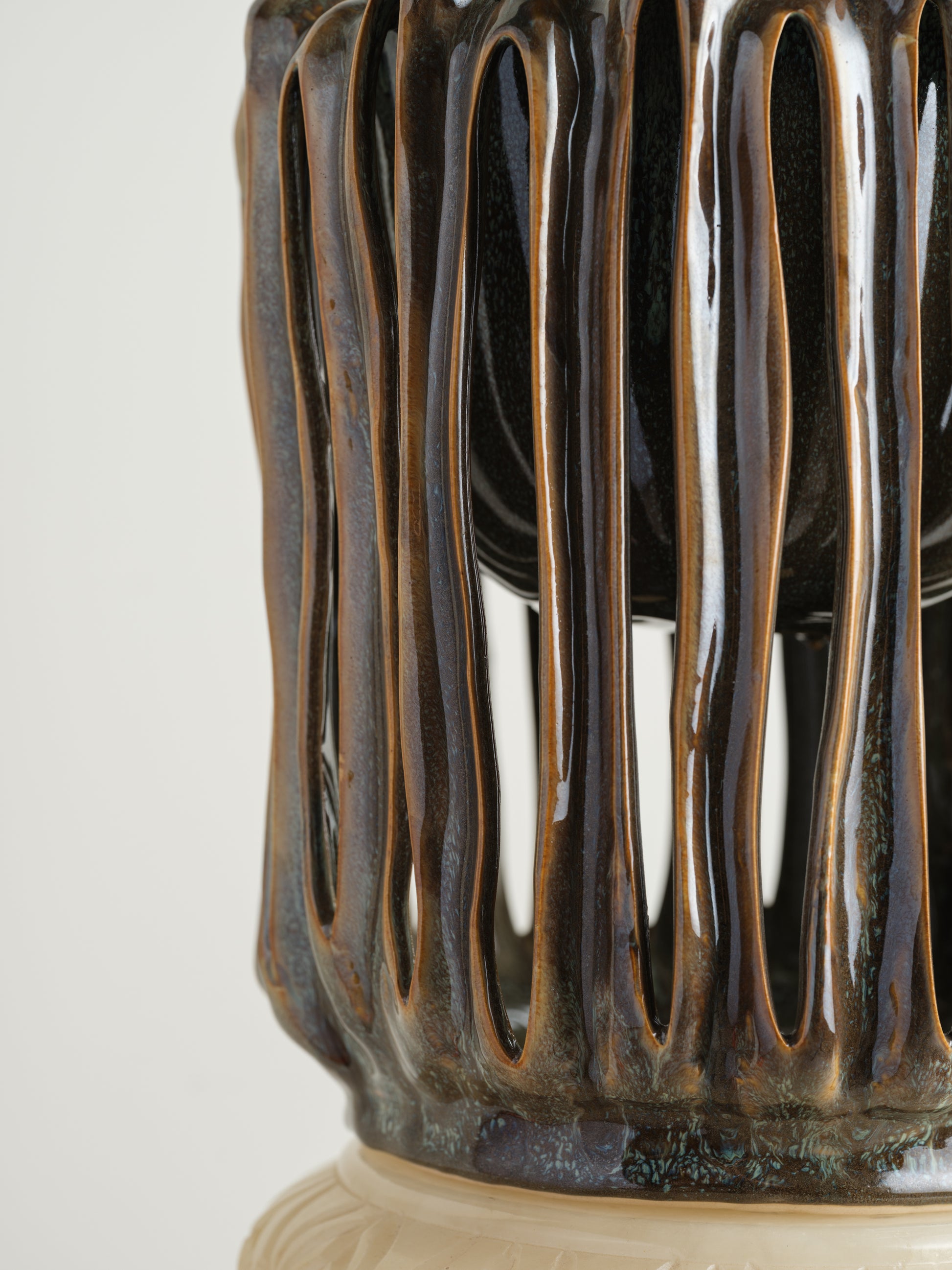 Ceramic vessel titled Drip Cage Vessel, featuring vertical dripping glaze lines forming an openwork cage-like structure with earthy brown and blue tones.