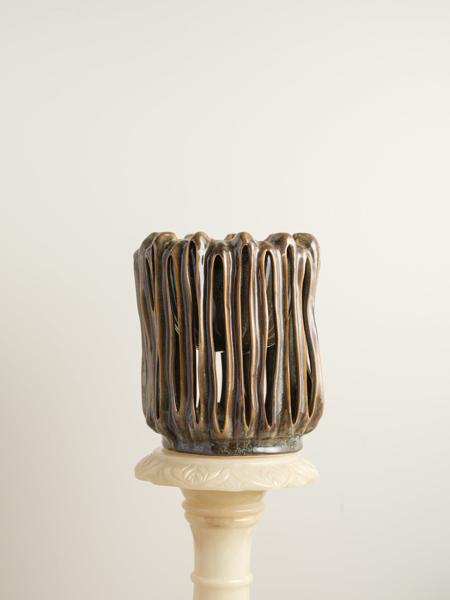 Ceramic vessel titled Drip Cage Vessel, featuring vertical dripping glaze lines forming an openwork cage-like structure with earthy brown and blue tones.