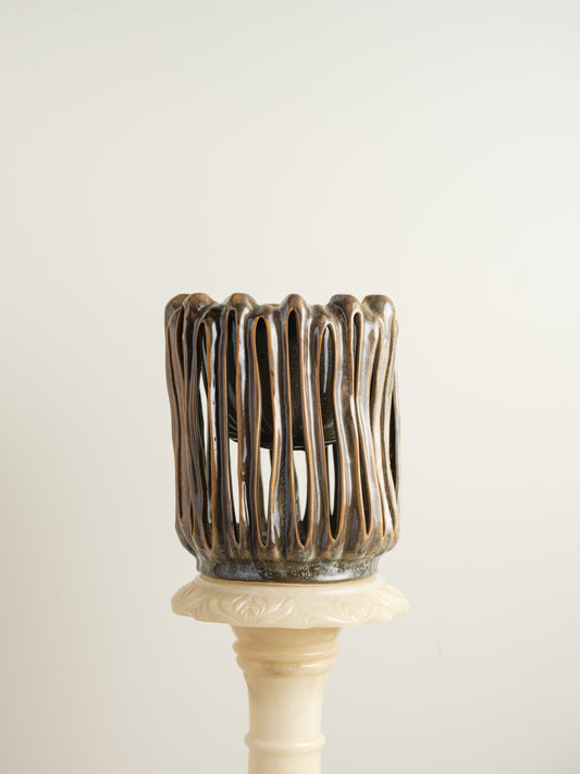 Ceramic vessel titled Drip Cage Vessel, featuring vertical dripping glaze lines forming an openwork cage-like structure with earthy brown and blue tones.