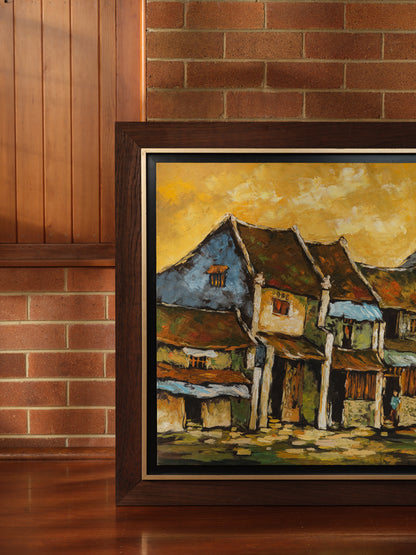 Oil painting titled Golden Eaves on Old Street, depicting a row of traditional houses with weathered tiled roofs under a golden-yellow sky, framed in dark wood.