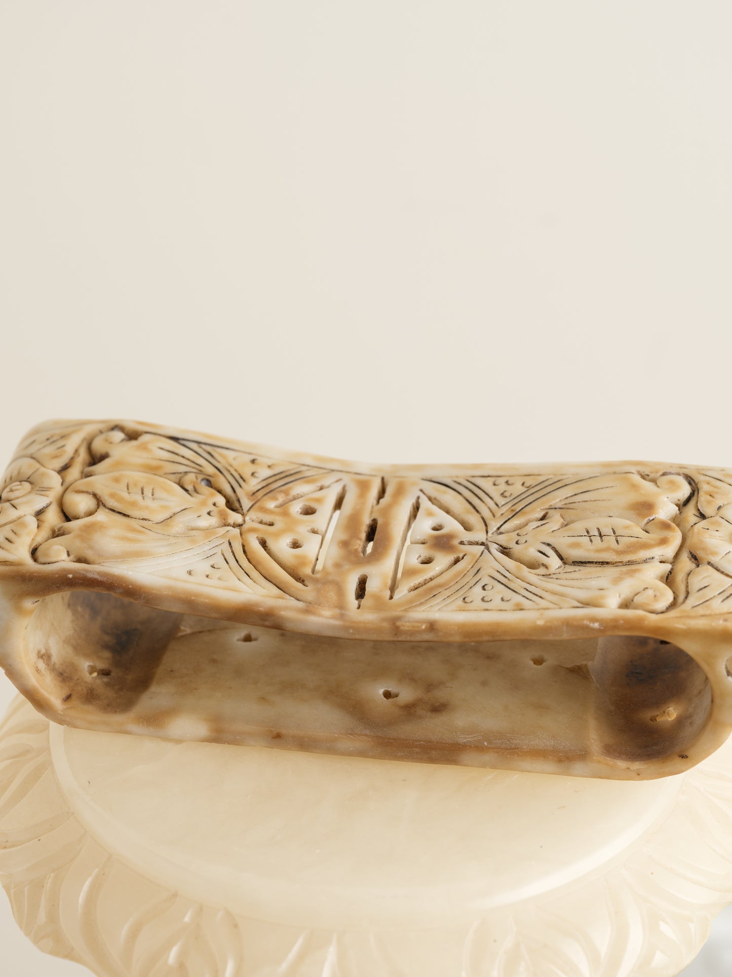 Ivory-toned pedestal stand with curved top and carved detailing, ideal for displaying vases or sculptures.