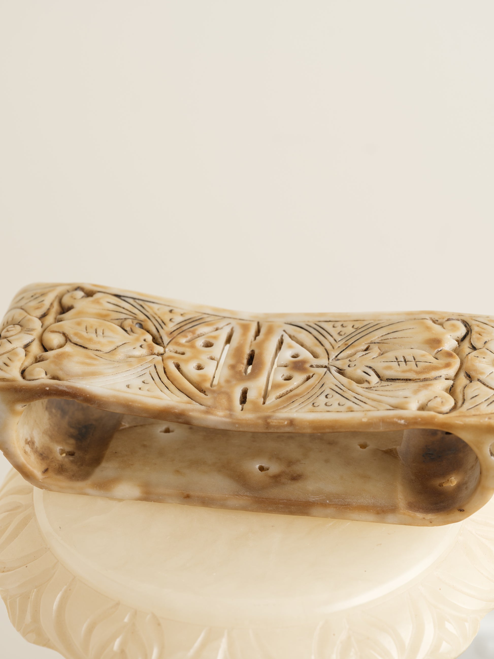 Ivory-toned pedestal stand with curved top and carved detailing, ideal for displaying vases or sculptures.