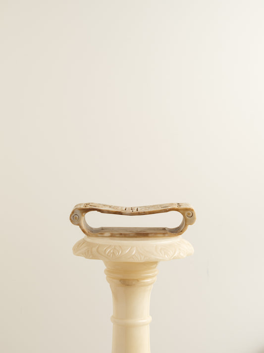 Ivory-toned pedestal stand with curved top and carved detailing, ideal for displaying vases or sculptures.