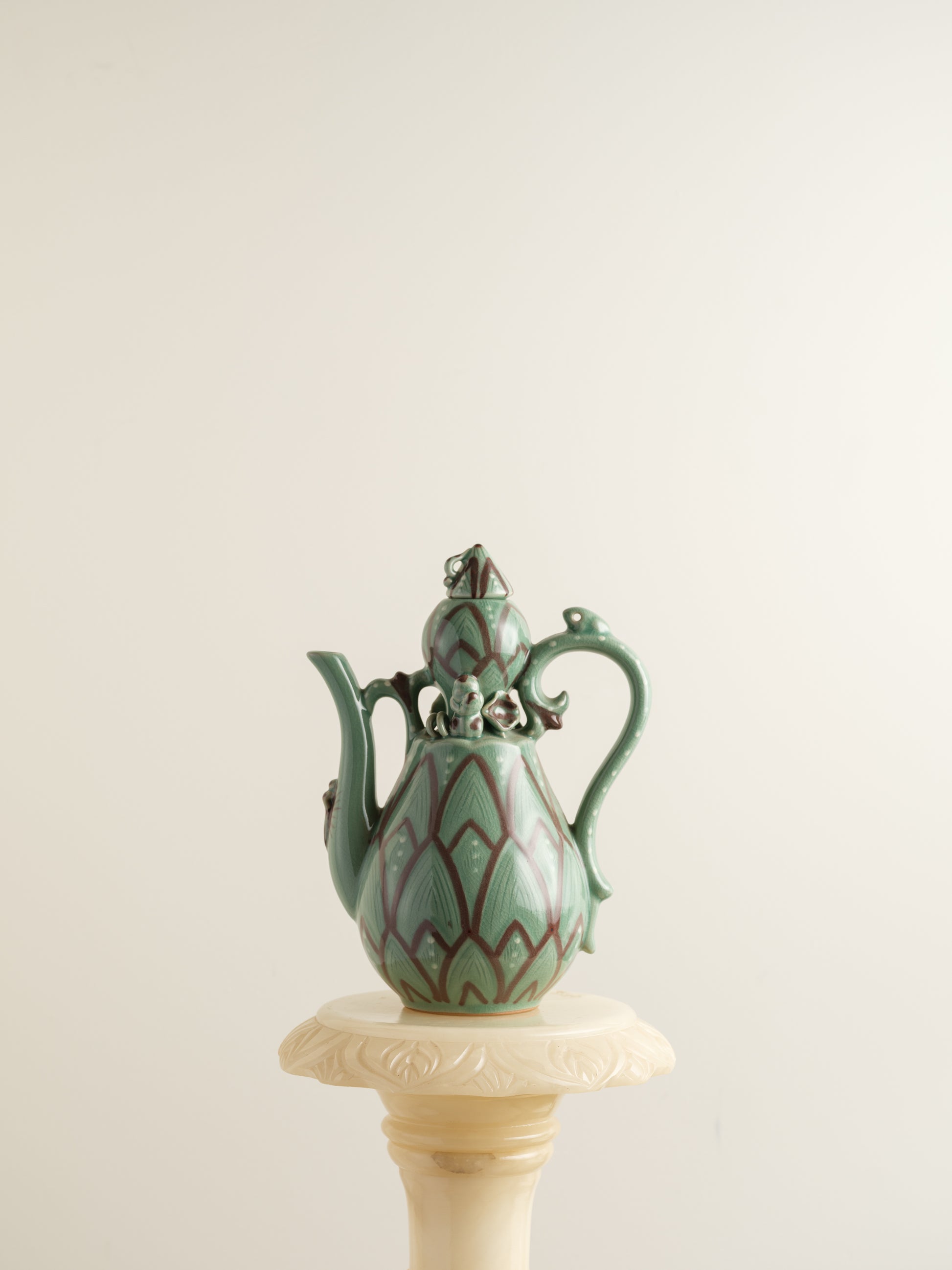 Celadon ewer with lotus petal relief design and sculpted handle and spout, finished in green glaze with brown accents.
