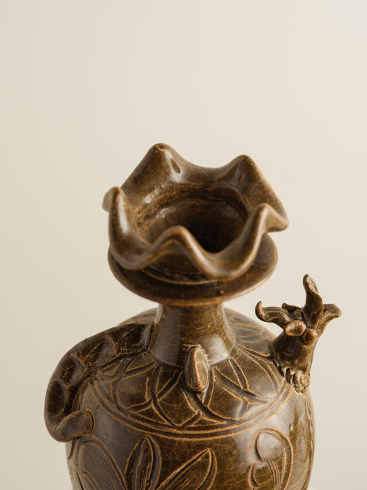 Brown stoneware ewer with carved lotus motif and flared crown-shaped mouth.

