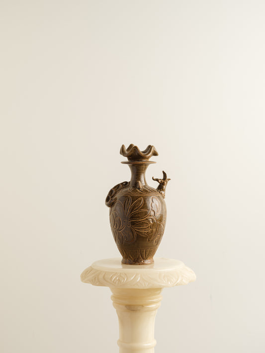 Brown stoneware ewer with carved lotus motif and flared crown-shaped mouth.
