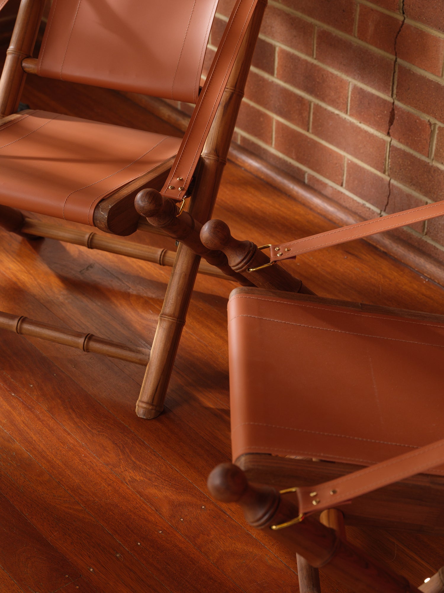 Replica faux bamboo and cognac leather safari style folding chair, vintage-inspired design, with brick wall