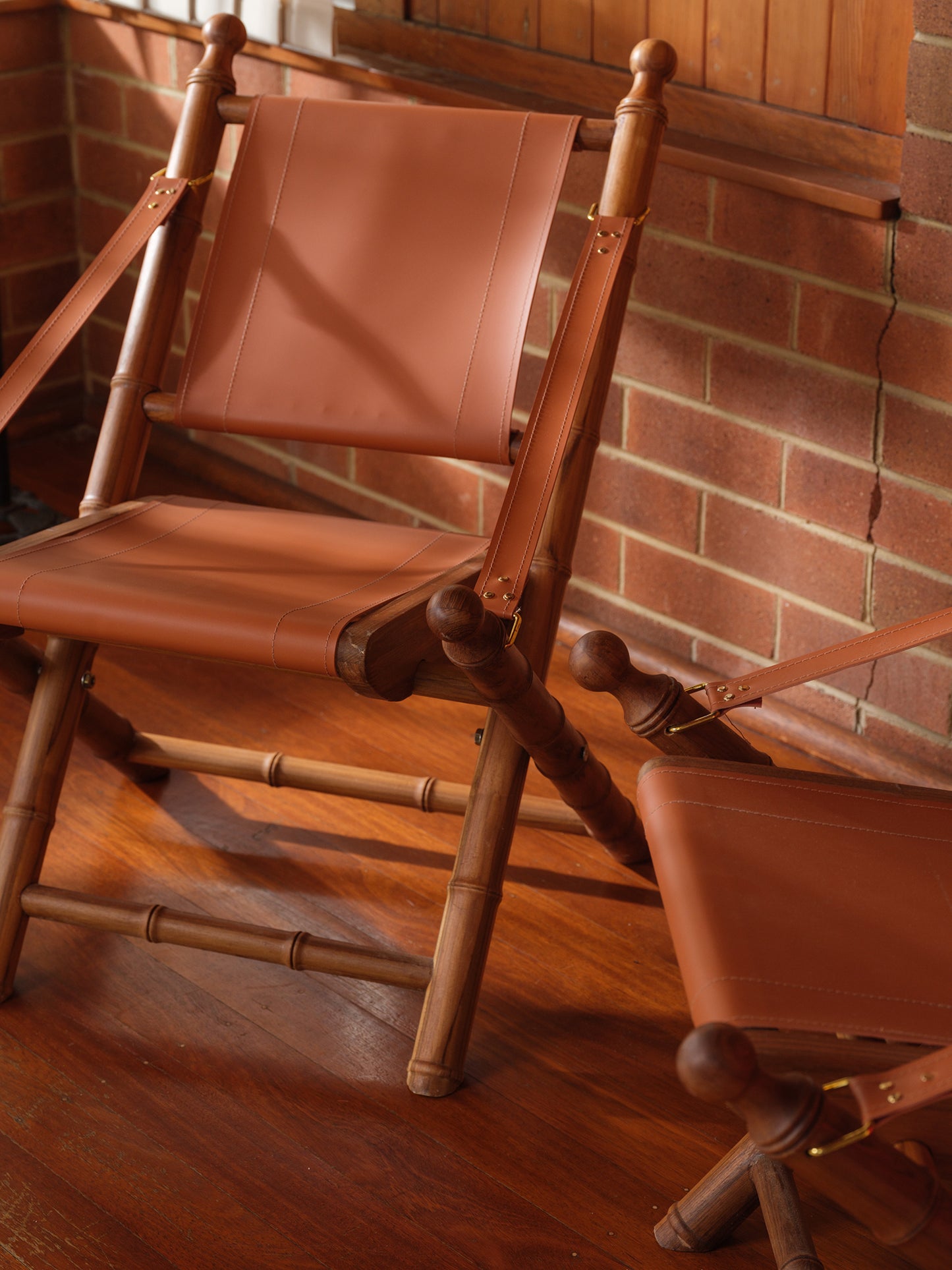 Replica faux bamboo and cognac leather safari style folding chair, vintage-inspired design, with brick wall