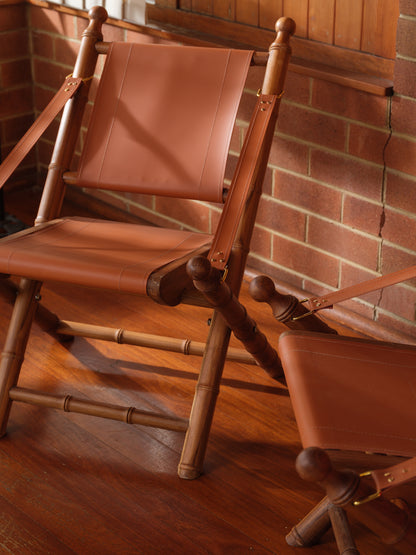 Replica faux bamboo and cognac leather safari style folding chair, vintage-inspired design, with brick wall
