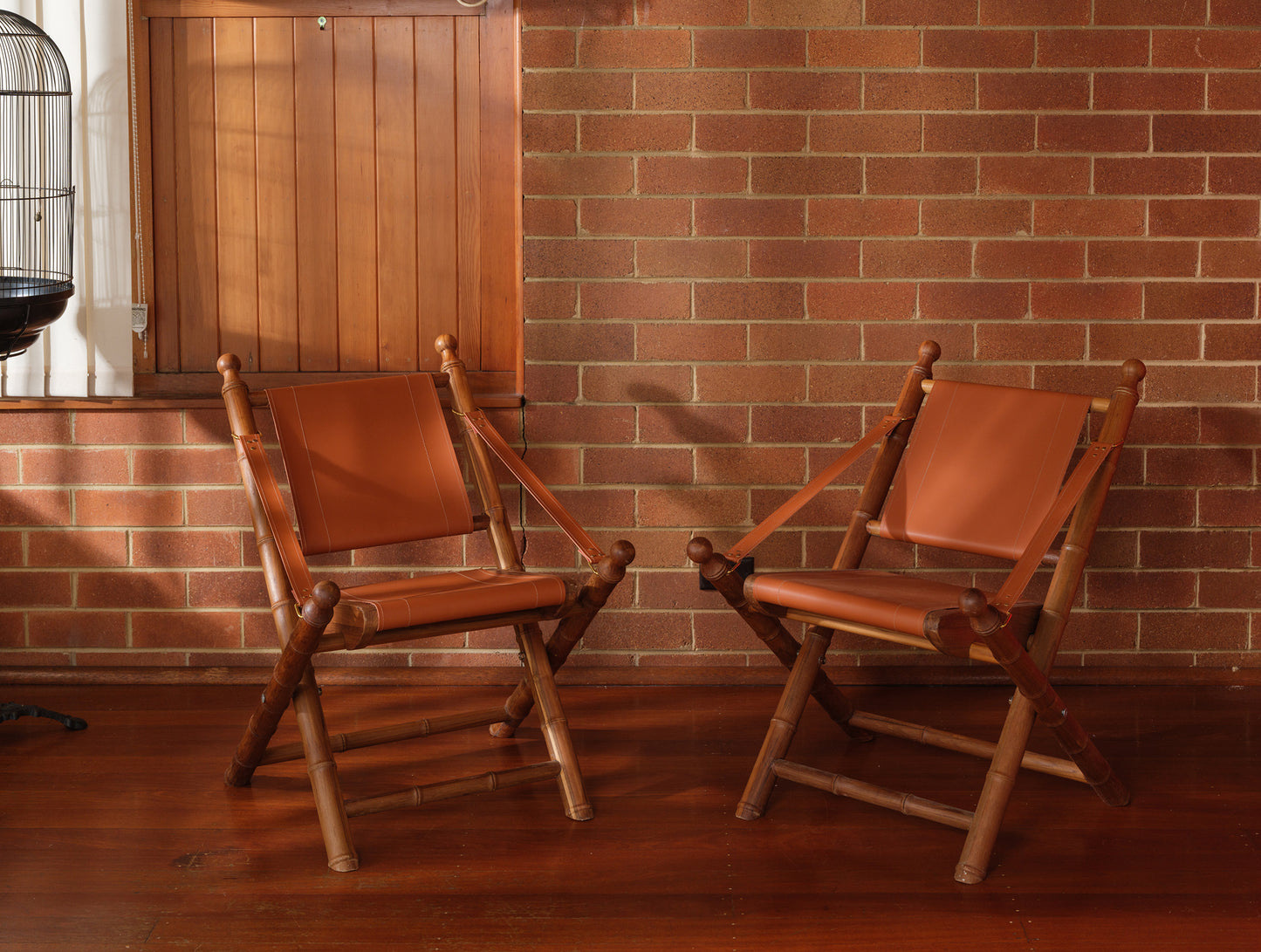 Replica faux bamboo and cognac leather safari style folding chair, vintage-inspired design, with brick wall