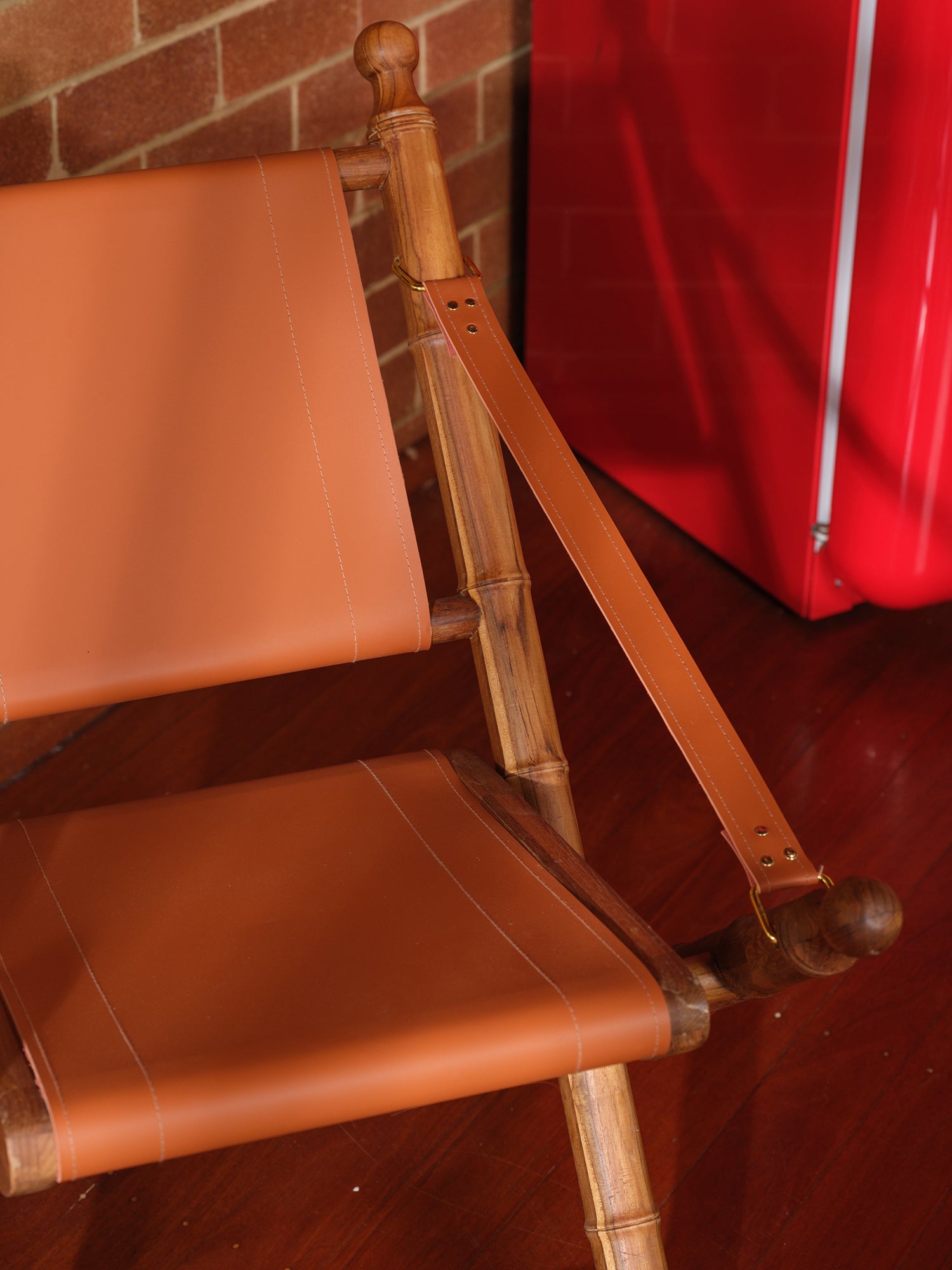 Replica faux bamboo and cognac leather safari style folding chair, vintage-inspired design, with brick wall