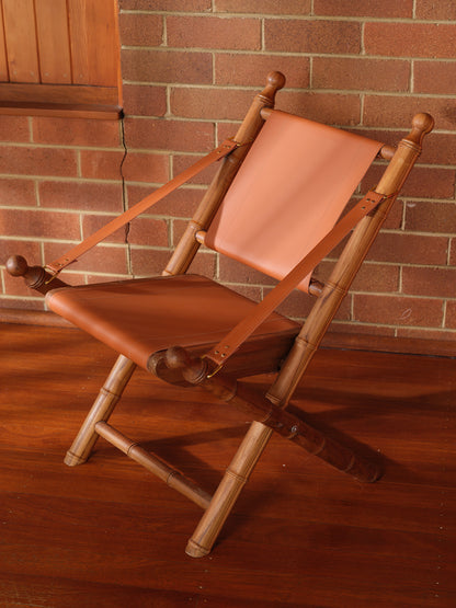 Replica faux bamboo and cognac leather safari style folding chair, vintage-inspired design, with brick wall