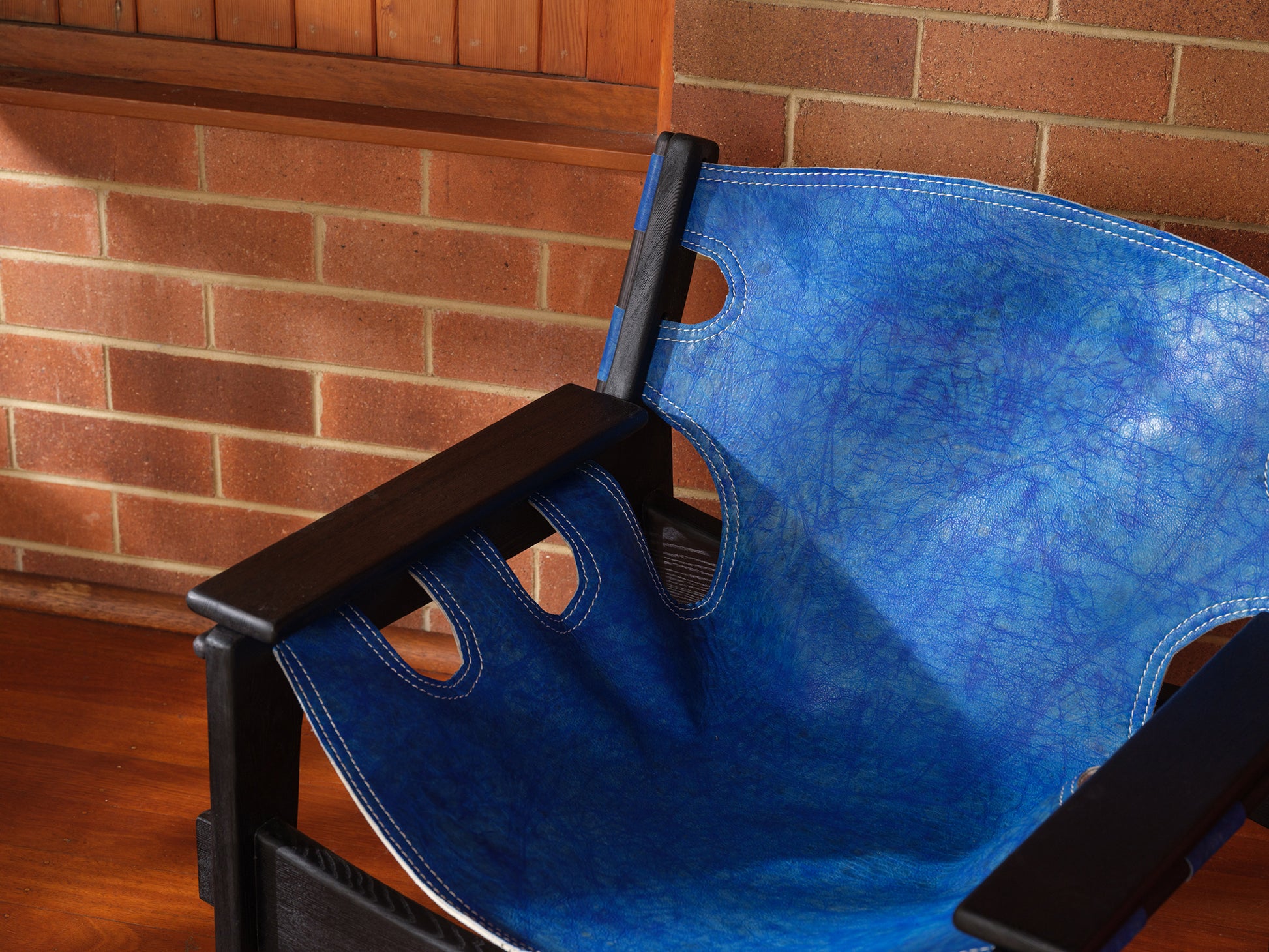 Replica Sergio Rodrigues Kilin lounge chair in blue leather with black wooden frame with brick wall