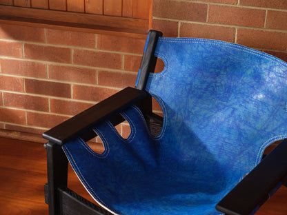 Replica Sergio Rodrigues Kilin lounge chair in blue leather with black wooden frame with brick wall