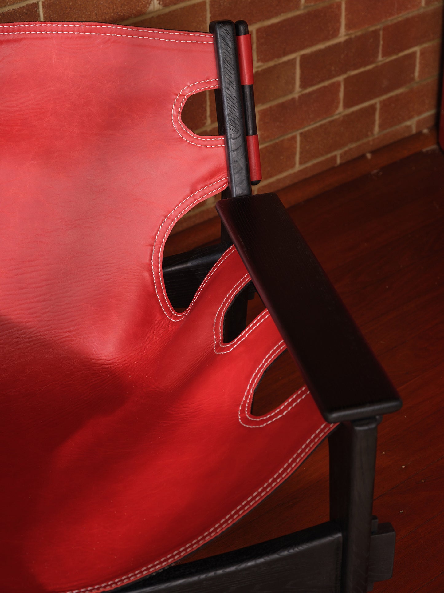Replica Sergio Rodrigues Kilin lounge chair in red leather with black wooden frame with brick wall background
