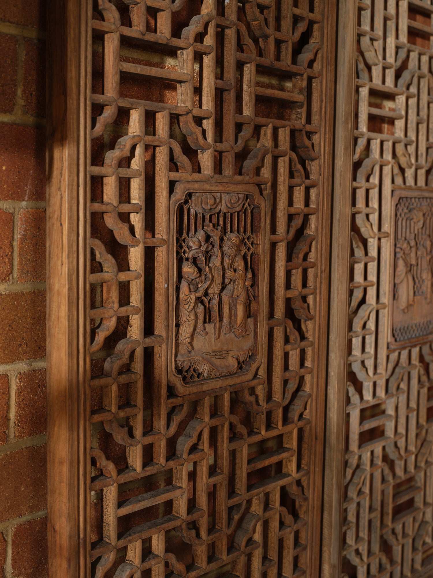 Pair of antique Chinese lattice panels with intricate geometric fretwork and carved scholar scenes in relief at the center.