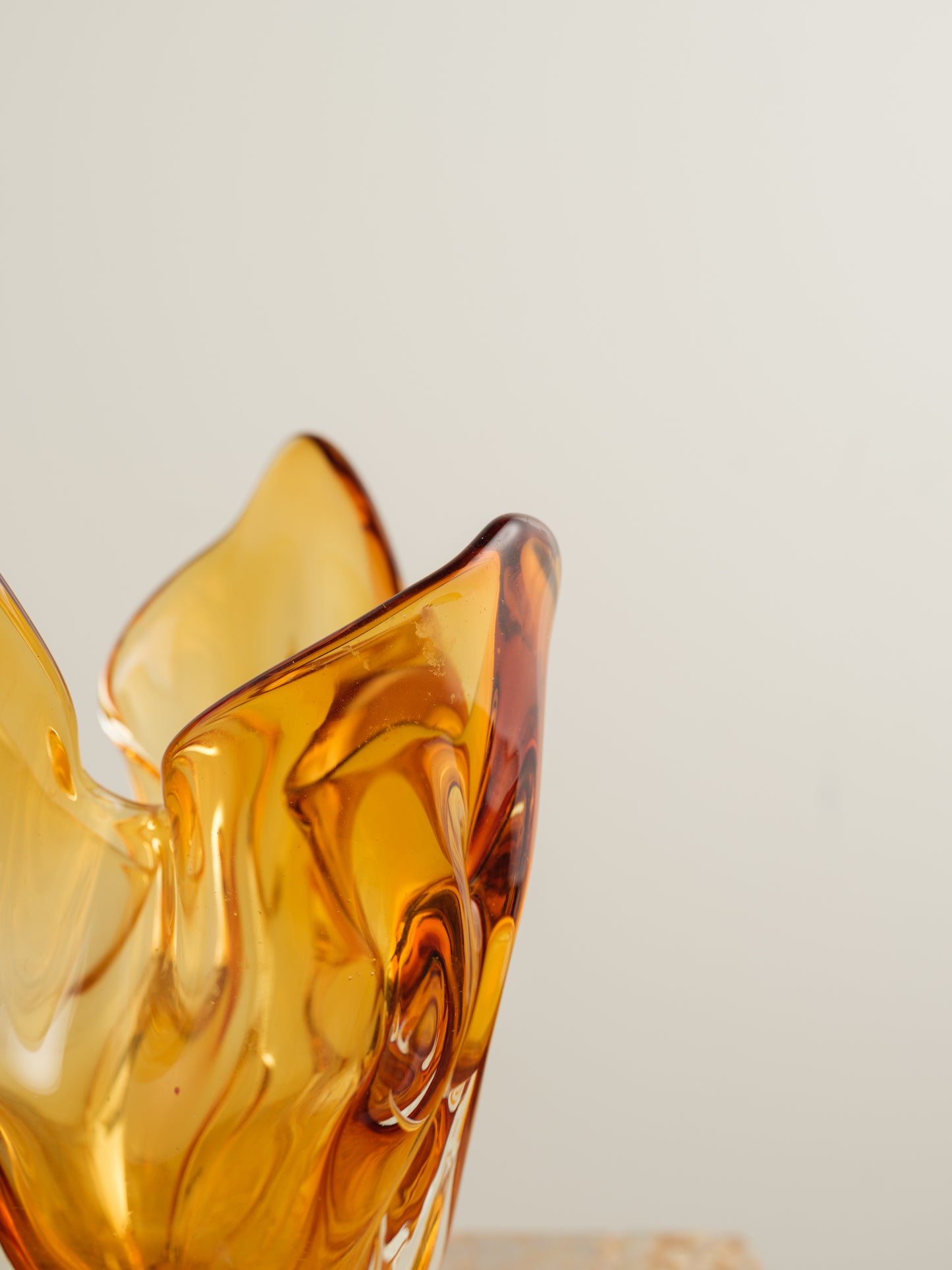 Amber-orange art glass vase with petal-like sculptural form and fluid edges.