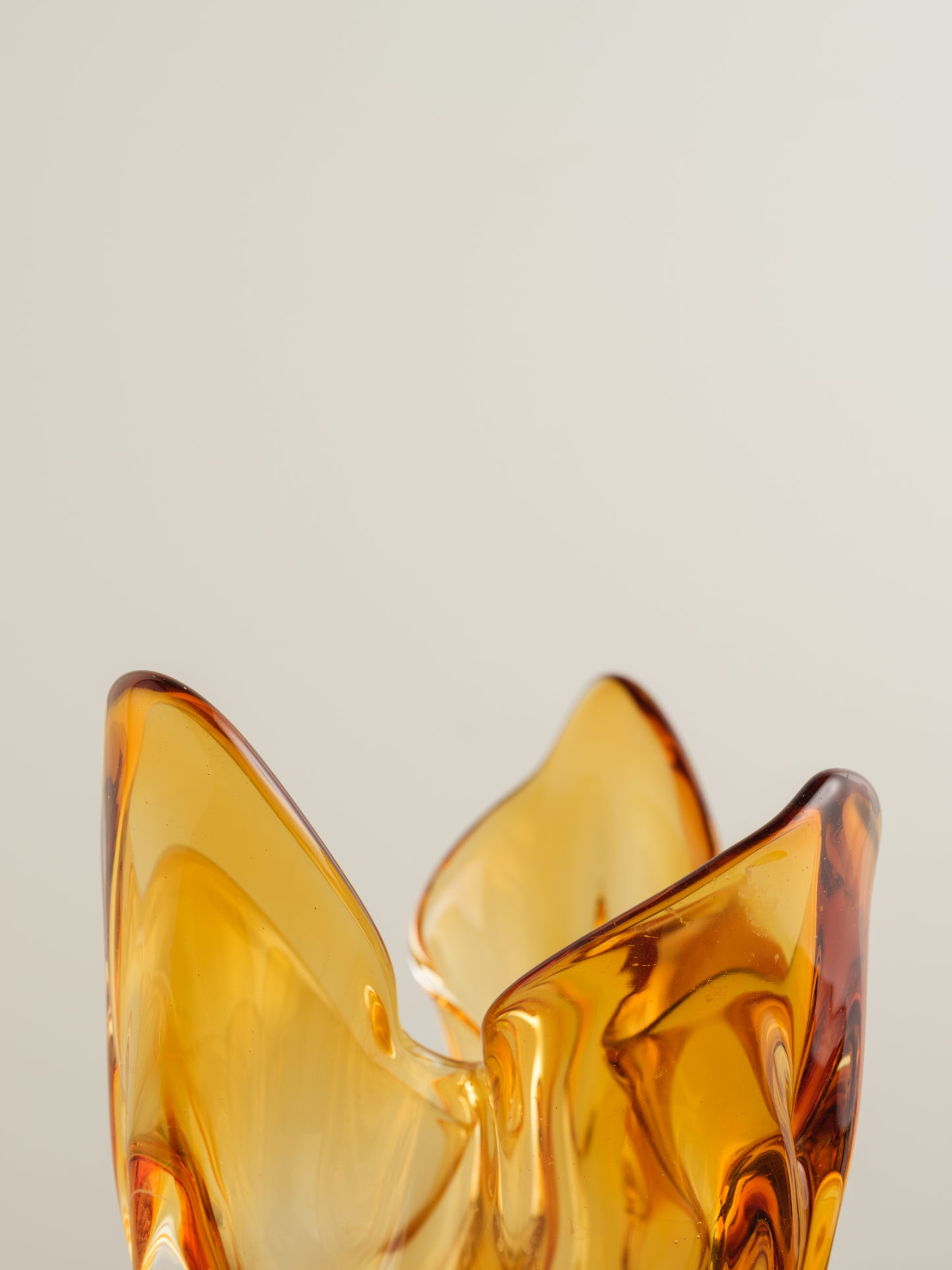 Amber-orange art glass vase with petal-like sculptural form and fluid edges.