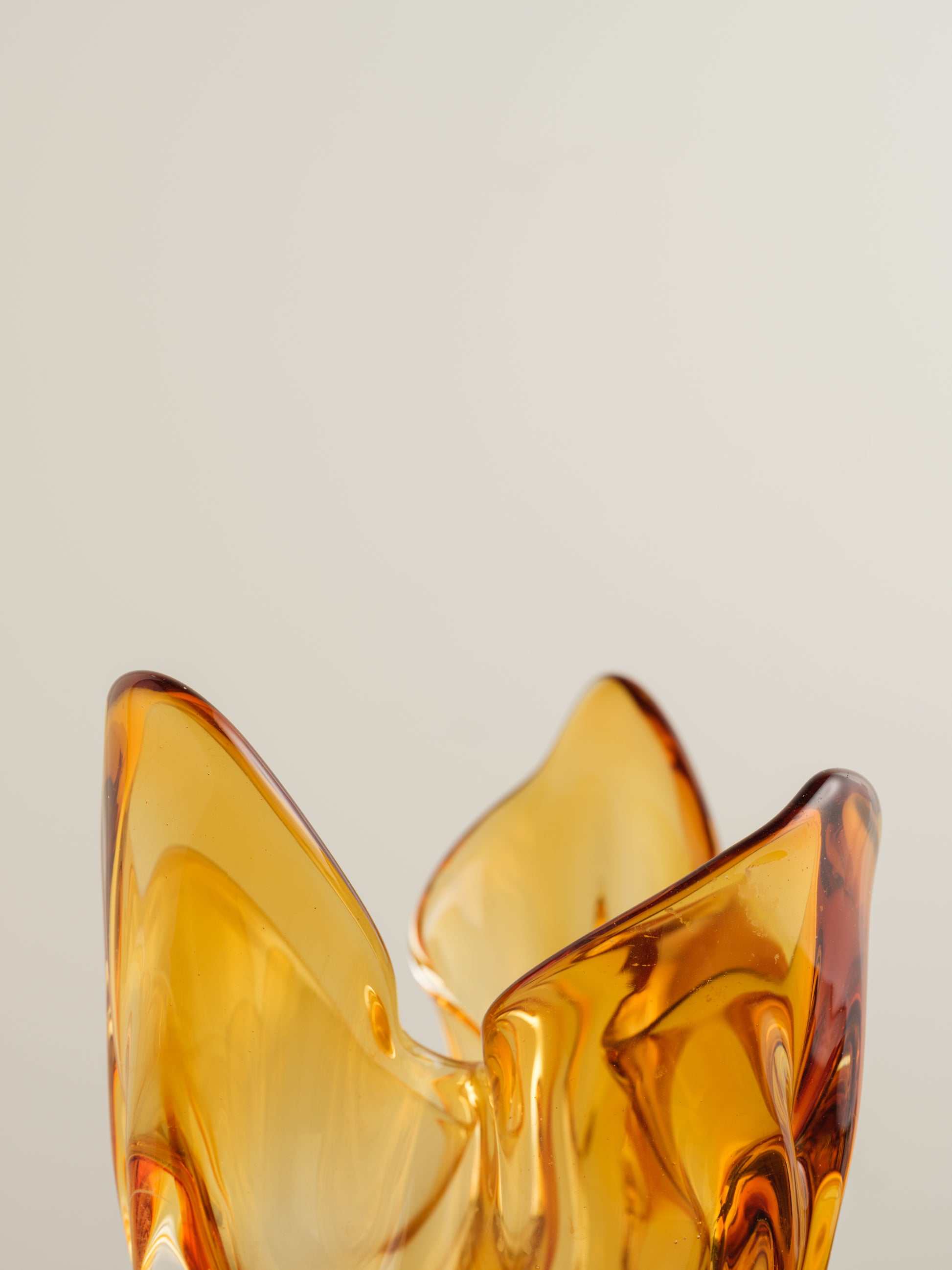 Amber-orange art glass vase with petal-like sculptural form and fluid edges.