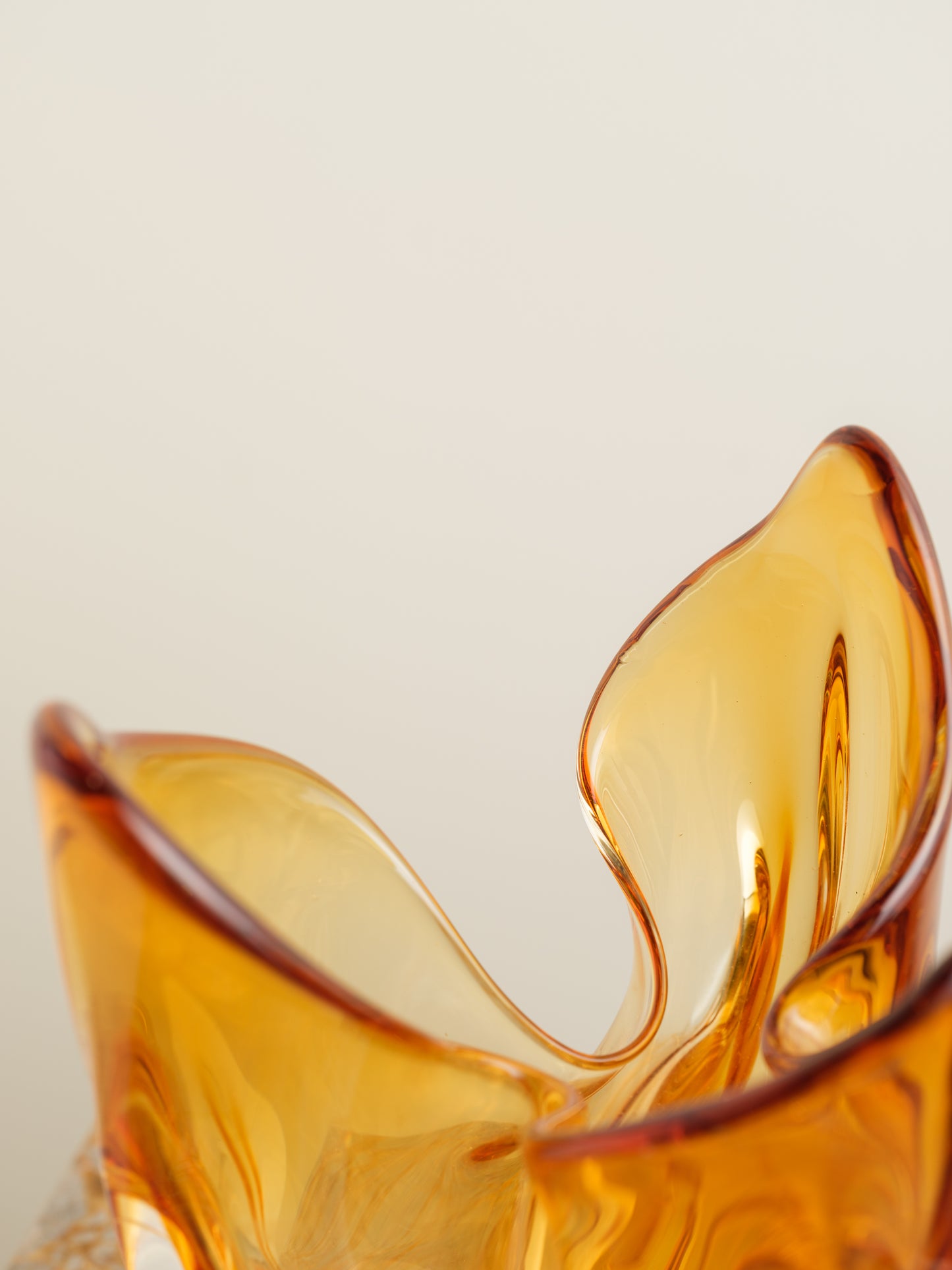 Amber-orange art glass vase with petal-like sculptural form and fluid edges.