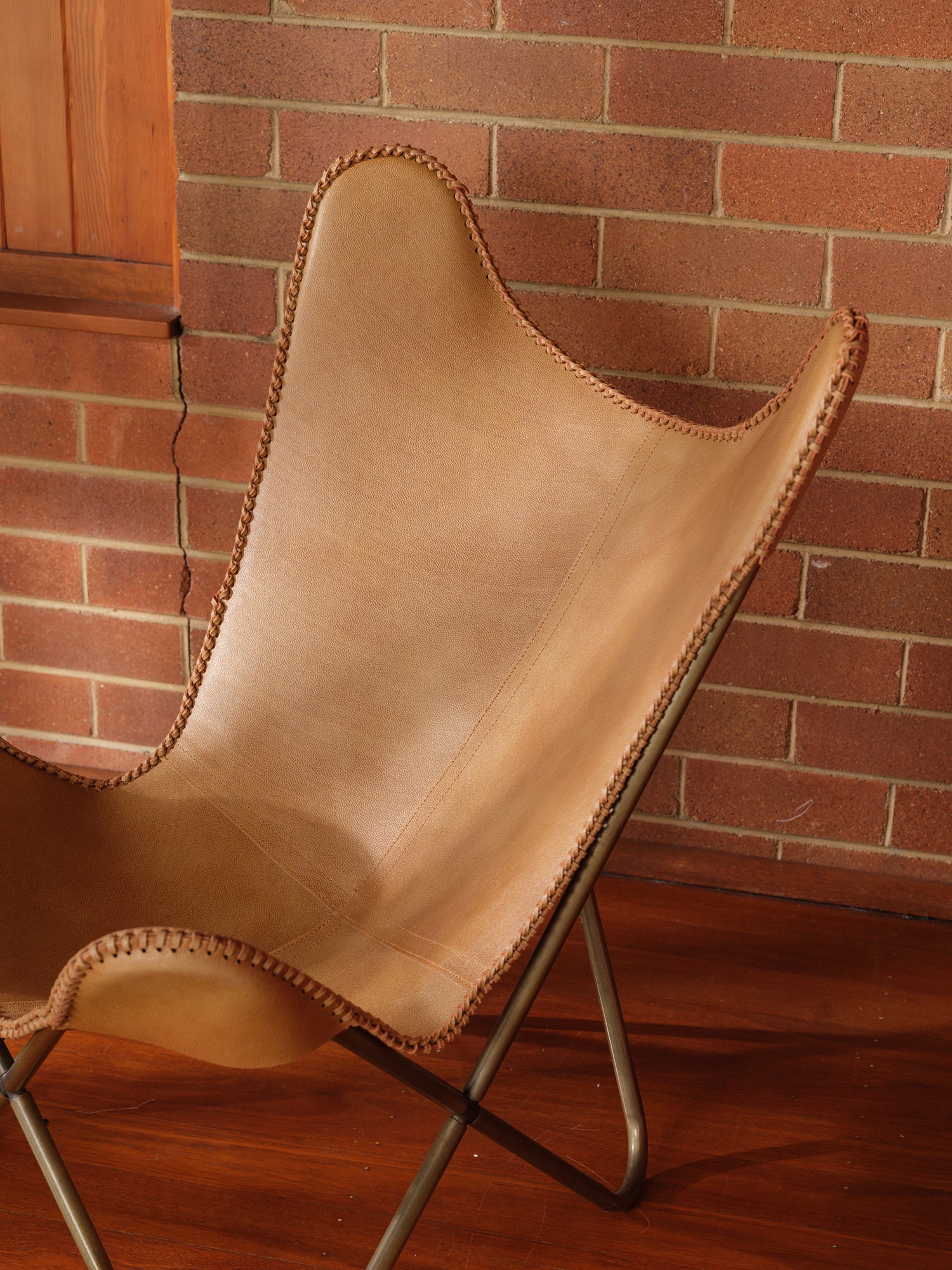 Tan suede butterfly lounge chair with stitched leather seat and metal frame, mid-century modern style