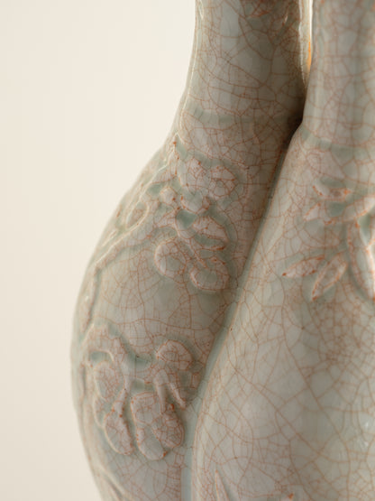 Celadon vase with three joined necks, embossed floral and bamboo motifs, and pale jade crackle glaze with russet tones.