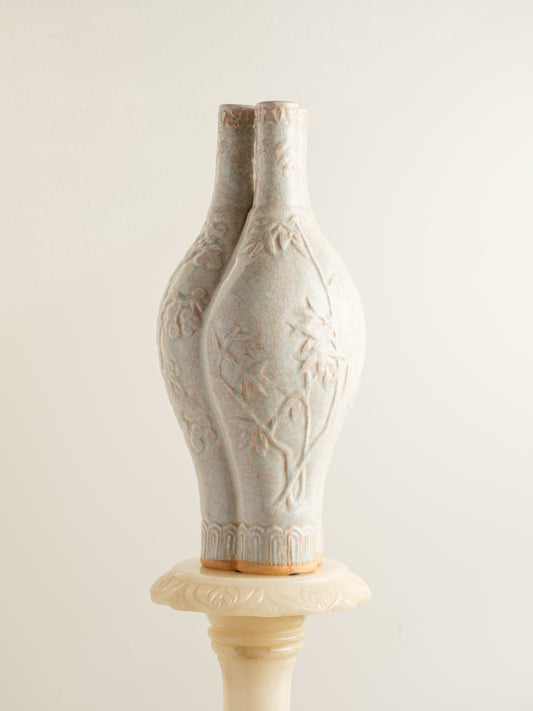 Celadon vase with three joined necks, embossed floral and bamboo motifs, and pale jade crackle glaze with russet tones.