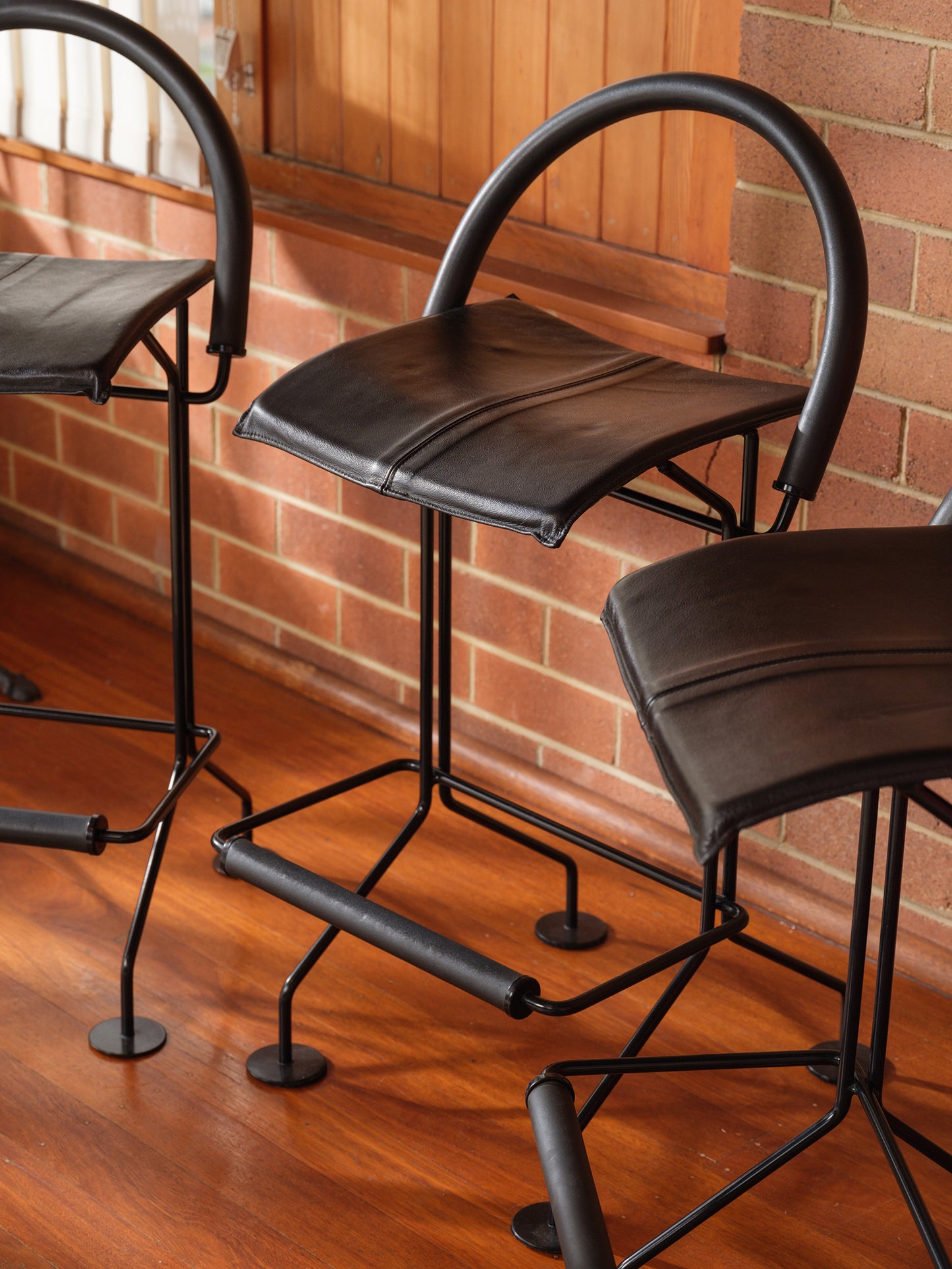 Vintage modern metal barstool with black leather seat and curved backrest.