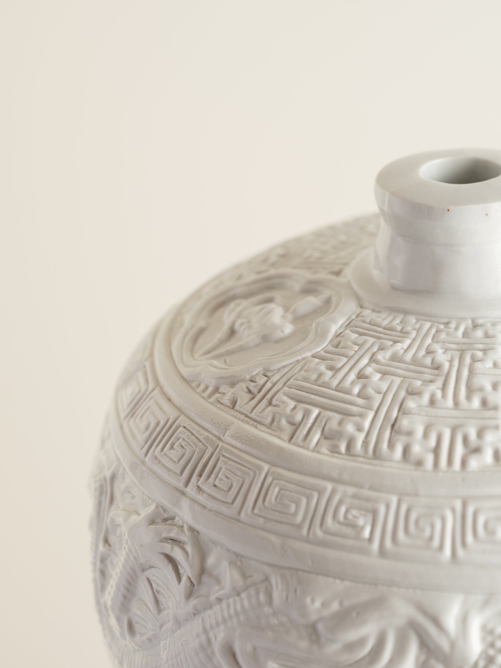 White porcelain meiping vase featuring intricate dragon relief motifs and geometric borders.