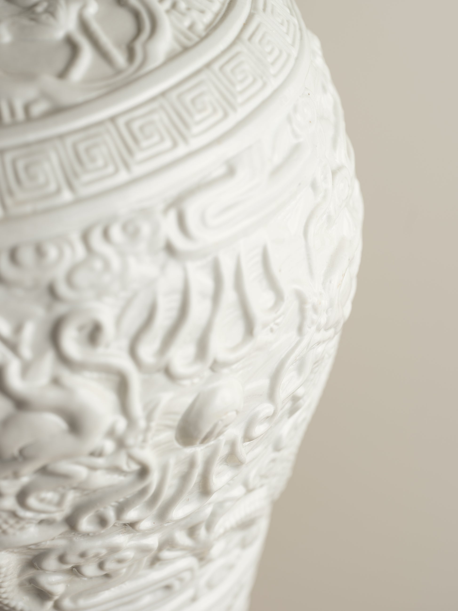White porcelain meiping vase featuring intricate dragon relief motifs and geometric borders.