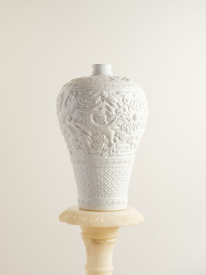 White porcelain meiping vase featuring intricate dragon relief motifs and geometric borders.