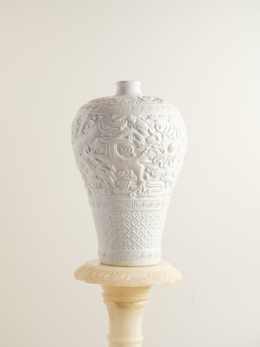 White porcelain meiping vase featuring intricate dragon relief motifs and geometric borders.